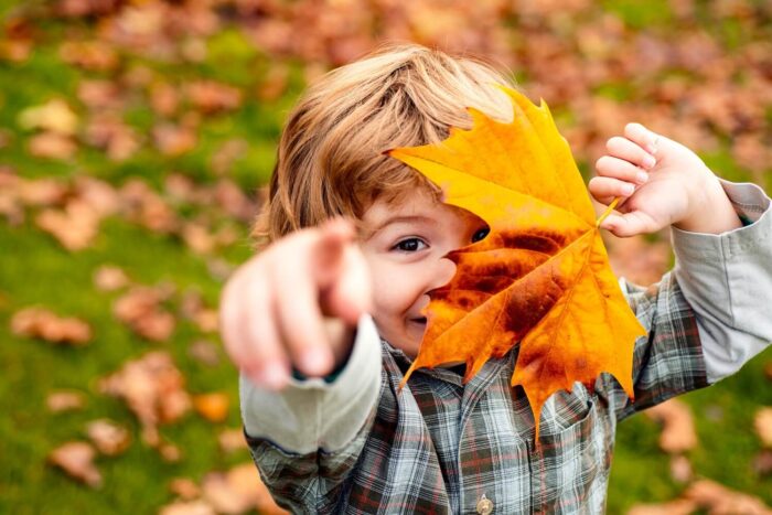 enfant qui pointe du doigt avec sa main et cache son visage avec une feuille d'érable orange