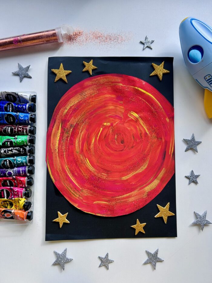 Planète Mars à la gouache découpée et collée sur un fond noir décoré d'étoiles dorées pailletées