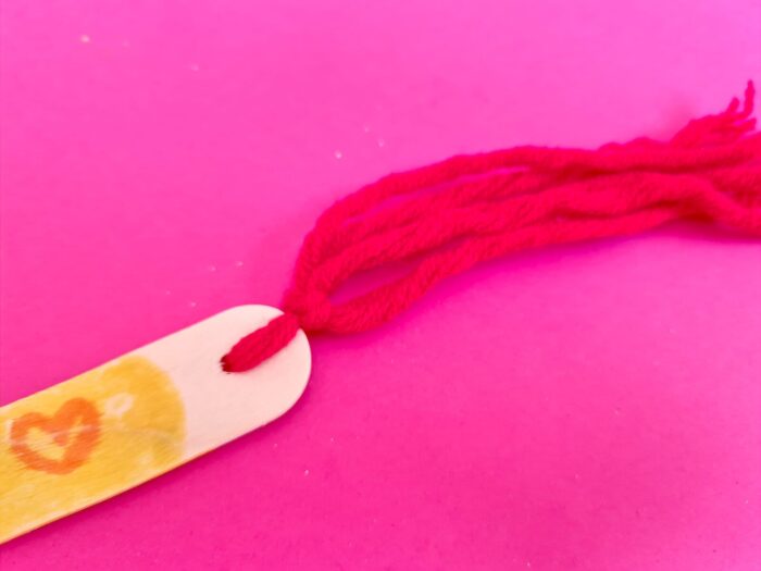 Nœud de laine rouge maintenant le pompon sur le marque-page crayon