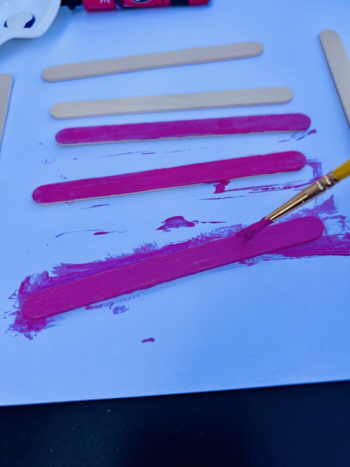 Enfant peignant des bâtonnets en bois en rose avec de la gouache Maped et un pinceau