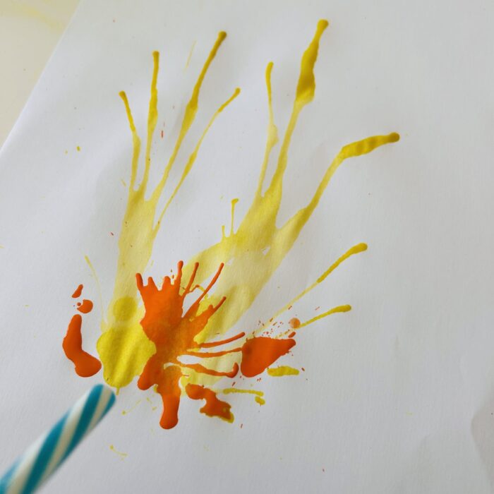 Peinture soufflée à la paille formant des filaments jaunes et orange sur le papier