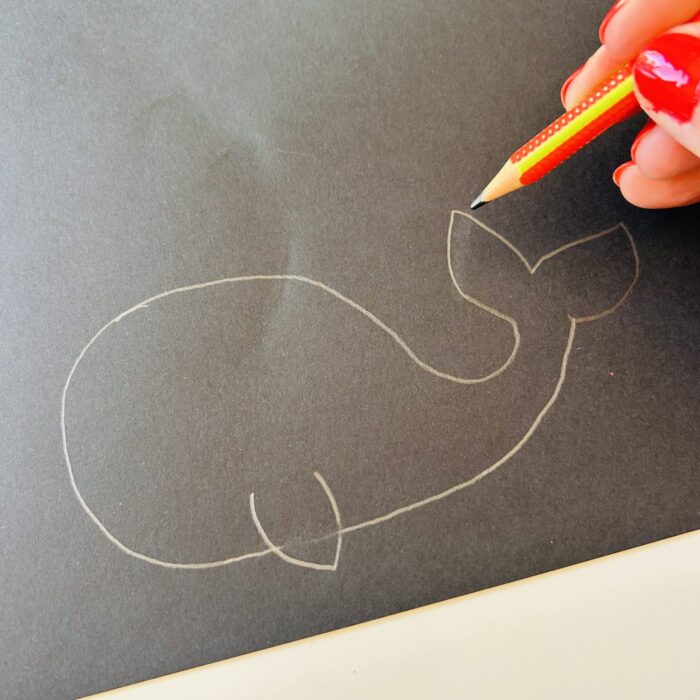 Silhouette de baleine dessinée au crayon sur une feuille cartonnée noire